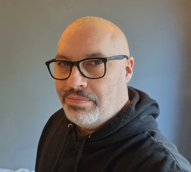 Christian Blackwell, speculative fiction author, wearing a black jacket against a dark background.